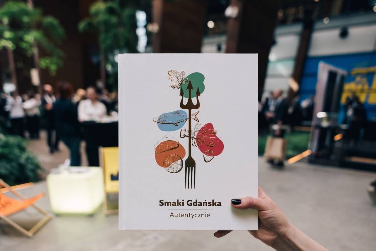 Ręka trzymająca książkę Smaki Gdańska wewnątrz budynku Europejskiego Centrum Solidarności.
